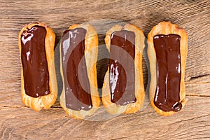 Eclairs with chocolate icing on wood background.