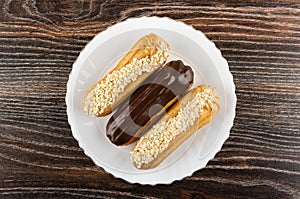 Eclairs with chocolate and peanut in plate on dark wooden table. Top view