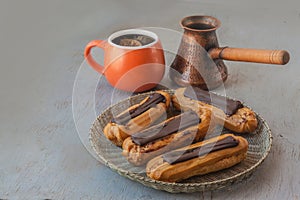 Eclairs and cup with cezve on gray background