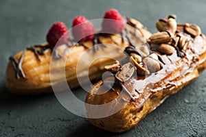 Eclairs with peanuts, chocolate icing and raspberries