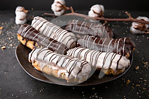 Eclairs or profiteroles with black chocolate and white chocolate with custard inside on a metal plate on a dark background.