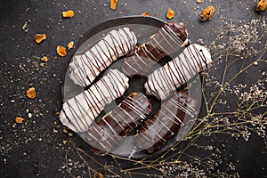 Eclairs or profiteroles with black chocolate and white chocolate with custard inside on a metal plate on a dark background.