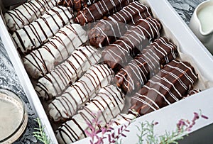 Eclairs or profiteroles with white and chocolate glaze in box and on the plate over grey wooden background with spring flowers.