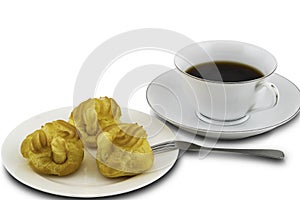 Eclairs in a white ceramic plate with metal folk and a cup of black coffee