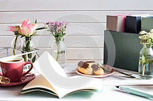 Eclairs on a white wooden table with cup of coffee, spring flowers and an open notebook with ink pencil.