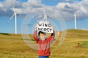 Eco activist boy with banner `Wind Energy` on background of power stations for renewable electric energy production