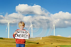 Eco activist boy with banner Wind Energy on background of power stations for renewable electric energy production.