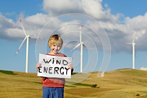 Eco activist boy with banner `Wind Energy` on background of power stations for renewable electric energy production.