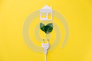 Eco, bio, energy-saving concept. Paper white house and electrical plug, green leaves on yellow background with copy space.