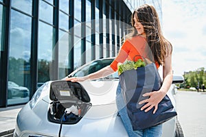 Eco electric car concept. Woman waiting electric car to charge.