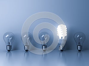 Eco energy saving light bulb , one glowing fluorescent lightbulb standing out from unlit incandescent bulbs reflection on blue