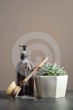 Eco-friendly amber glass soap bottle, wooden dish brush and succulent on dark marble background, sustainable homecare