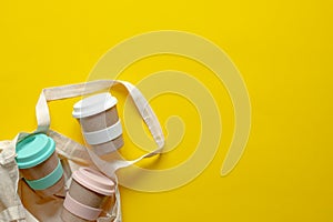 Eco-friendly bamboo cup and linen bag on a yellow background. Place for text.