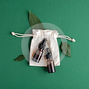 Eco-friendly bio cosmetics set on green background. Zero waste beauty products - serum amber glass dropper bottles and cotton bag
