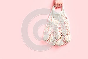 Eco-friendly concept with wooden eggs in cotton bag on pink background. Easter holiday