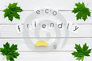 Eco friendly copy with green maple leaves, car figure and lamp for ecology concept on white wooden background top view