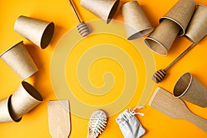 Eco friendly disposable paper cups, wooden kitchen tools, hairbrush cotton bag on yellow background. Copy space. Eco fast food. No