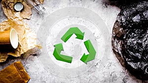 Eco-friendly life. Green paper recycling sign among waste paper, plastic, glass, polyethylene on grey background top