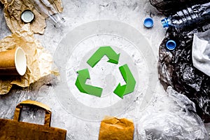 Eco-friendly life. Green paper recycling sign among waste paper, plastic, glass, polyethylene on grey background top