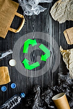 Eco-friendly life. Green paper recycling sign among waste paper, plastic, glass, polyethylene on grey wooden background