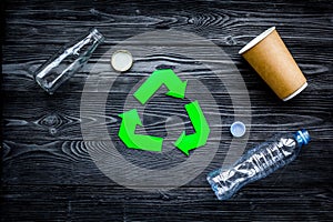 Eco-friendly life. Green paper recycling sign among waste paper, plastic, glass, polyethylene on grey wooden background