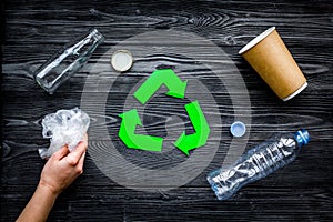 Eco-friendly life. Green paper recycling sign among waste paper, plastic, glass, polyethylene on grey wooden background