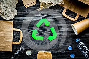 Eco-friendly life. Green paper recycling sign among waste paper, plastic, glass, polyethylene on grey wooden background