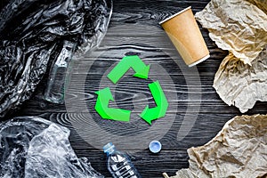 Eco-friendly life. Green paper recycling sign among waste paper, plastic, glass, polyethylene on grey wooden background