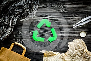 Eco-friendly life. Green paper recycling sign among waste paper, plastic, glass, polyethylene on grey wooden background