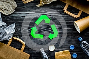 Eco-friendly life. Green paper recycling sign among waste paper, plastic, glass, polyethylene on grey wooden background