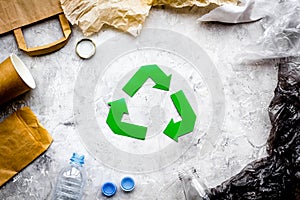 Eco-friendly life. Green paper recycling sign among waste paper, plastic, polyethylene on grey background top view