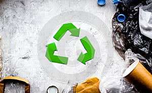 Eco-friendly life. Green paper recycling sign among waste paper, plastic, polyethylene on grey background top view copy