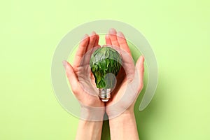 Eco-friendly light bulb with green leaves in woman`s hands. Saving energy, protecting the environment and conserving resource