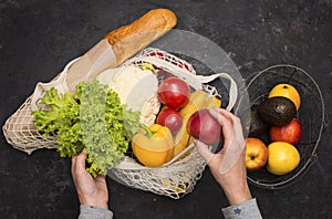 Eco friendly mesh bag with fruit and veggies on black background. No plastic. Zero waste and plastic free concept. Woman hands