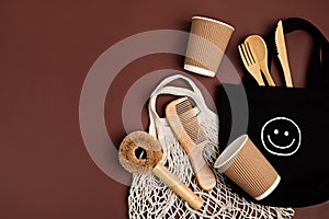 Eco friendly mug, brush, hair comb, wooden cutlery and cloth shopping bags on brown background. Zero waste sustainable