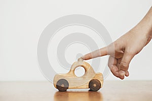 Eco friendly plastic free toy for toddler. Hand playing with natural wooden car toy on table on white wall background. Space for