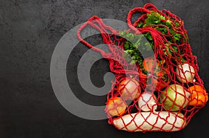 Eco friendly reusable mesh string bag with fresh organic vegetables on black background. Zero waste shopping concept