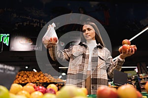 Eco friendly woman buys apples in the supermarket. Female grocery shopper opposes the use of plastic bags.