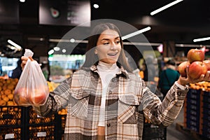 Eco friendly woman buys apples in the supermarket. Female grocery shopper opposes the use of plastic bags.