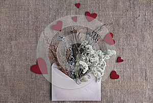 Eco-friendly zero waste valentine card. Craft paper envelope with dried sustainable flowers and cardboard handmade red hearts on