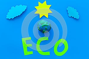 Eco icon cutout near plastiline symbol of planet Earth, sun, clouds on blue background top view copy space