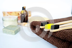 Eco natural bamboo toothbrush on white background with toiletries, natural soap, scrub, body brush and soft broun towel