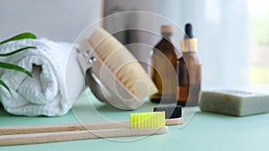 Eco natural bamboo toothbrush with toothpaste on green background with toiletries, natural soap, body brush and waffle