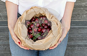 Eco package full of ripe red cherries in women`s hands on jeans