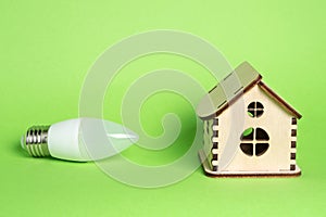 Eco power concept. LED bulb and toy wooden house on green background