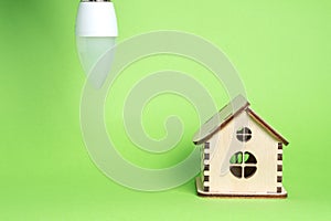 Eco power concept. LED bulb and toy wooden house on green background