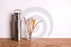 Eco set with bamboo cutlery, reusable water bottle on wooden background.