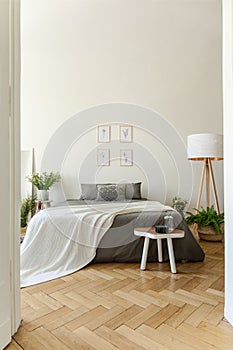 Eco style bedroom interior with a bed dressed in graphite linen and vanilla blanket. Herringbone wooden floor and high ceiling roo