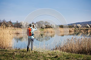 Eco tourism. Woman hiker with binoculars watching birds and wildlife animals at lake