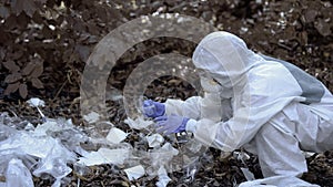 Eco volunteer in protective clothes crumpling plastic cup, studying pollution